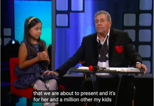 Image of Jerry Lewis with his hand on the knee of a little girl in a wheelchair. The caption except says "that we are about to present and it's for her and a million other my kids"
